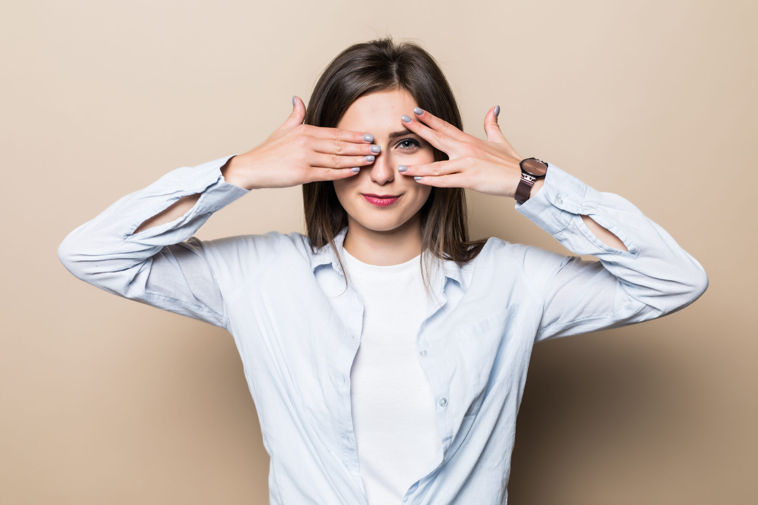 Young woman cover eyes while standing isolated on beige background