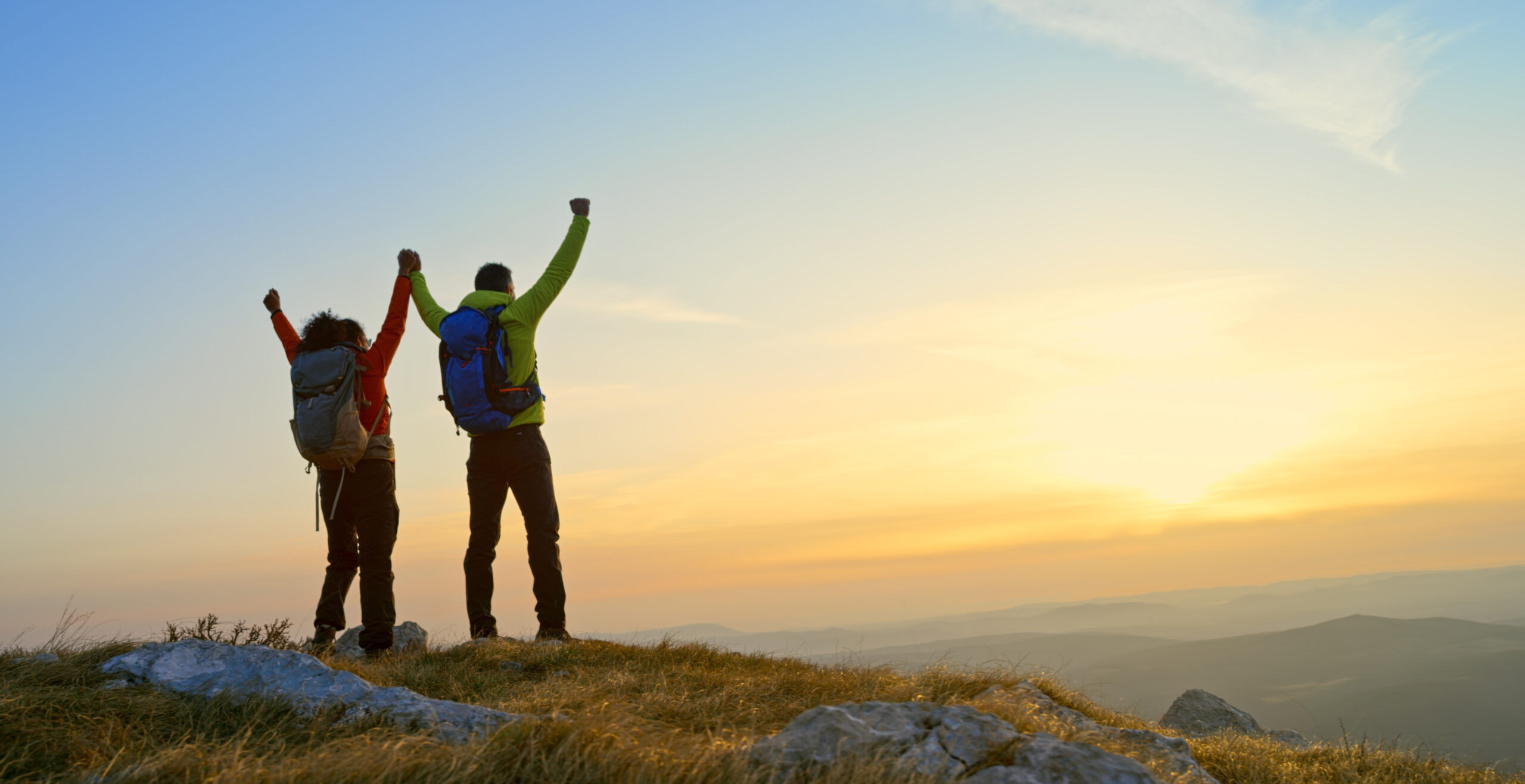 Rear view of mature couple holding hands while standing on mountain during sunset.